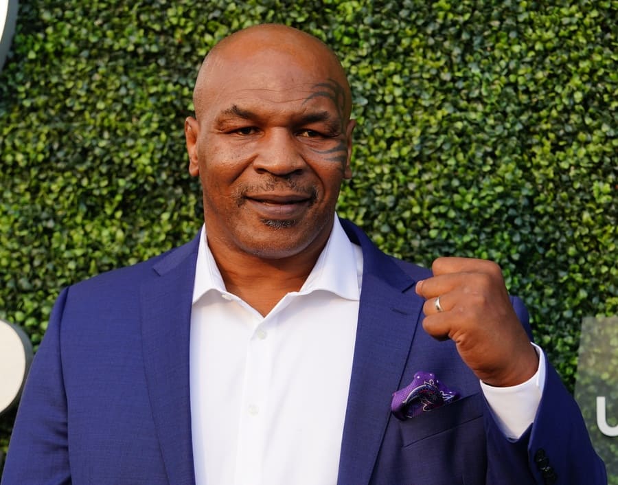 Mike Tyson making a fist standing in front of some bushes.