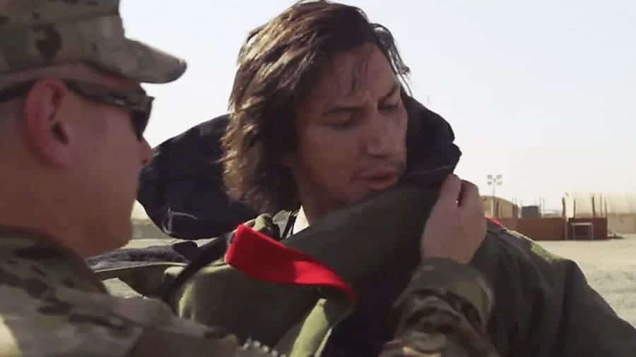 Adam Driver is trying on a bomb vest with military personnel. 