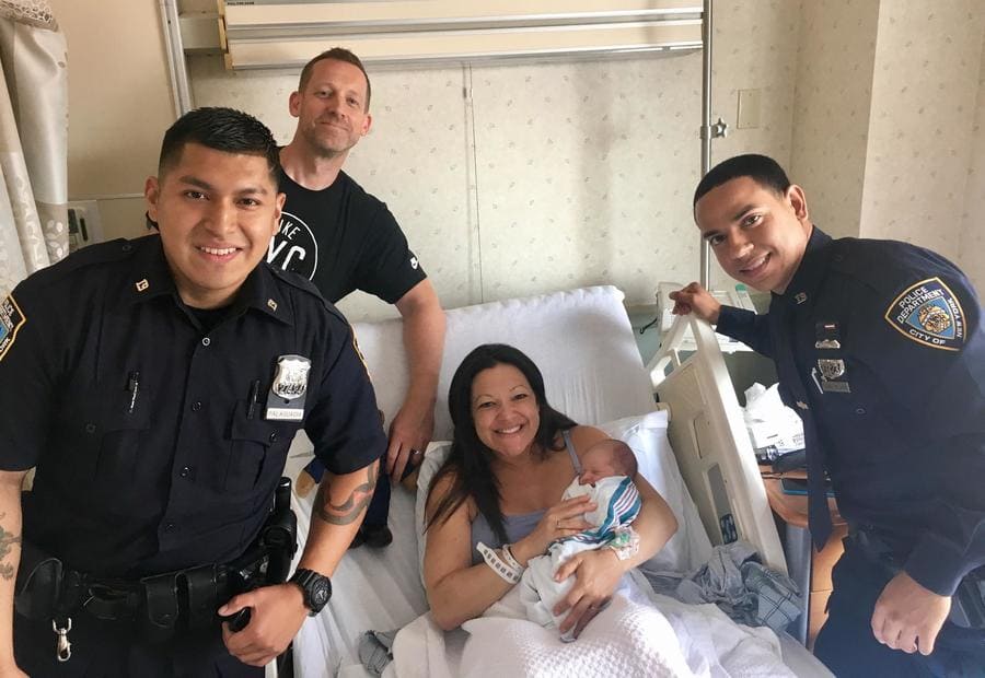 Police officers standing next to a woman in a hospital bed after her giving birth.