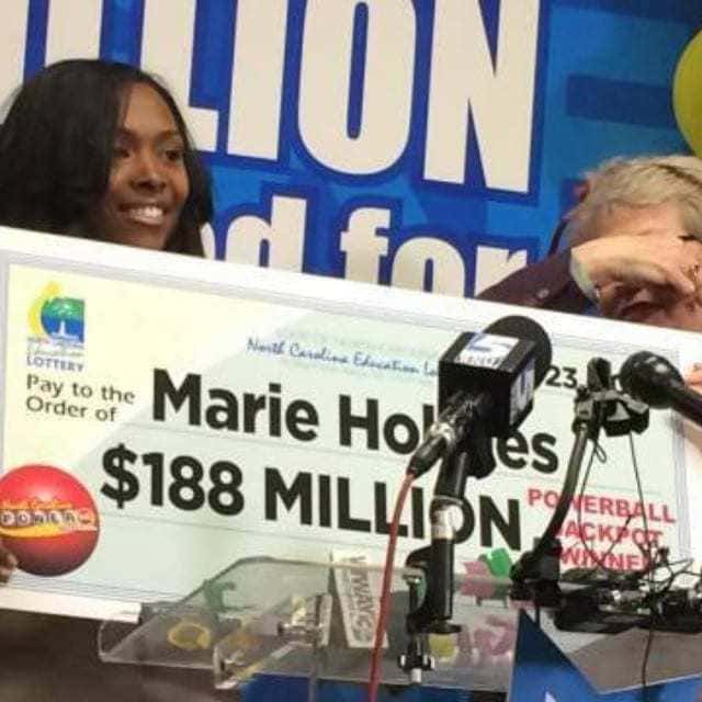 Marie Holmes is pictured above behind a podium with microphones holding her large lottery check for $188 Million.