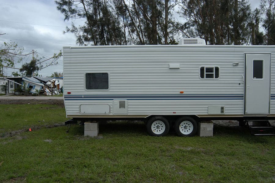 A white trailer not hooked up to a car and held in place by a few concrete blocks.