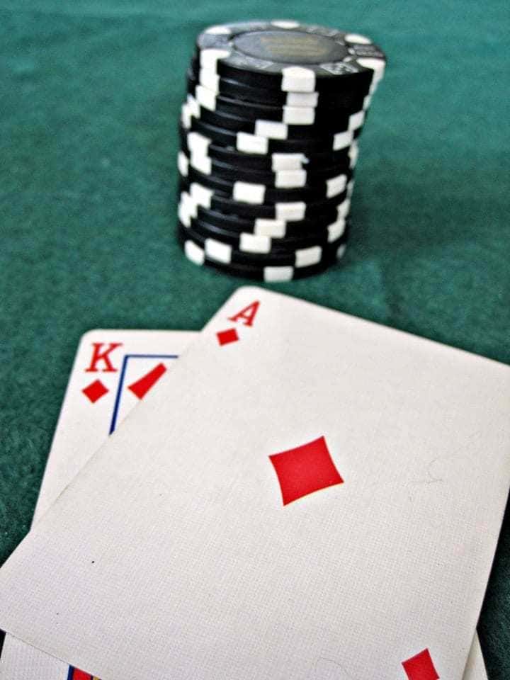 Photograph of a stack of black and white poker chips placed next to a King and Ace of diamonds on a green felt background.