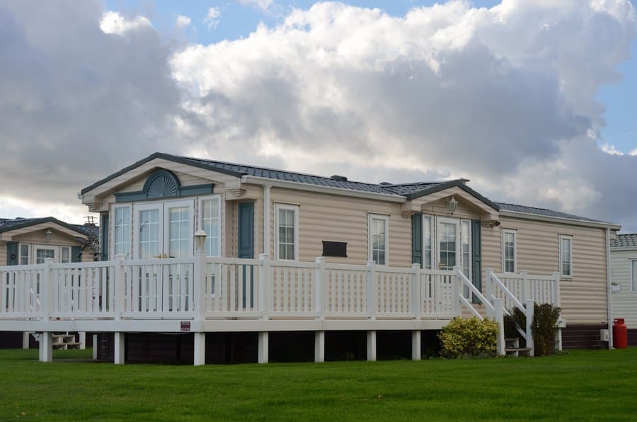 A cream-colored trailer with a gray roof and shutters, and a small porch attached.