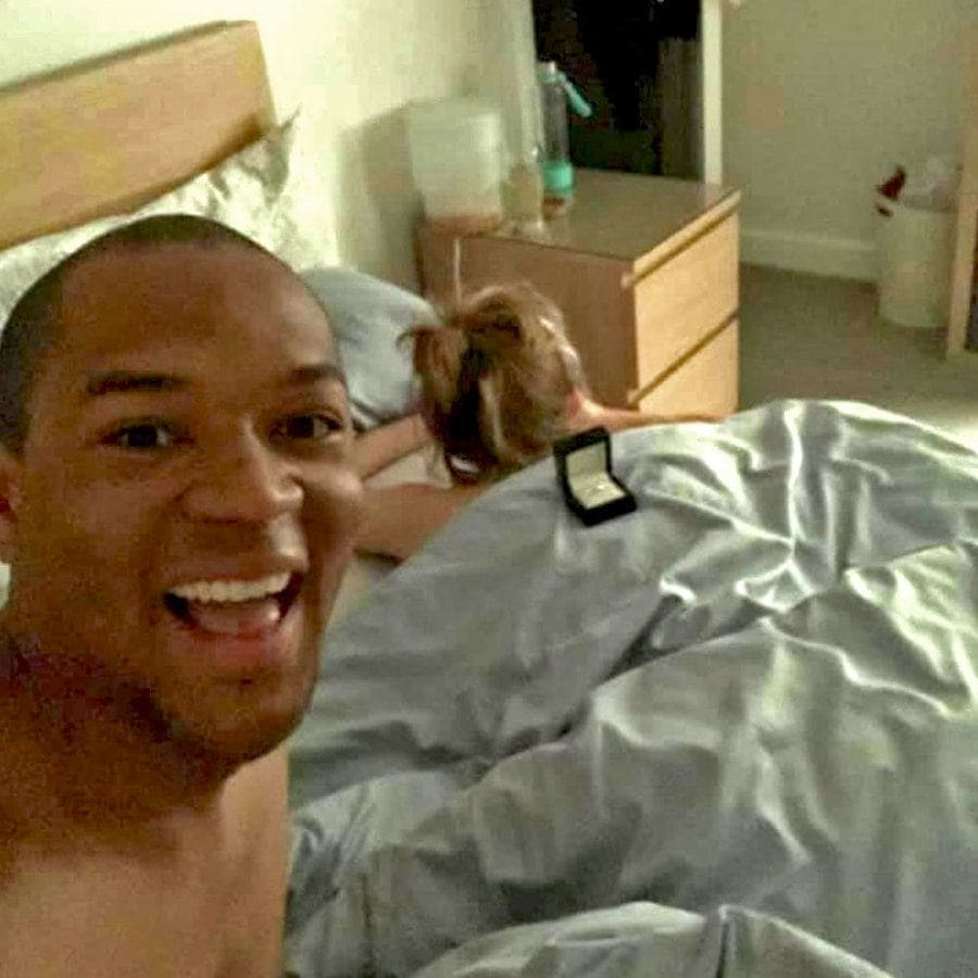 Cally lying stomach down under the covers on their bed with the engagement ring sitting on her back, and Edi is taking a selfie. 