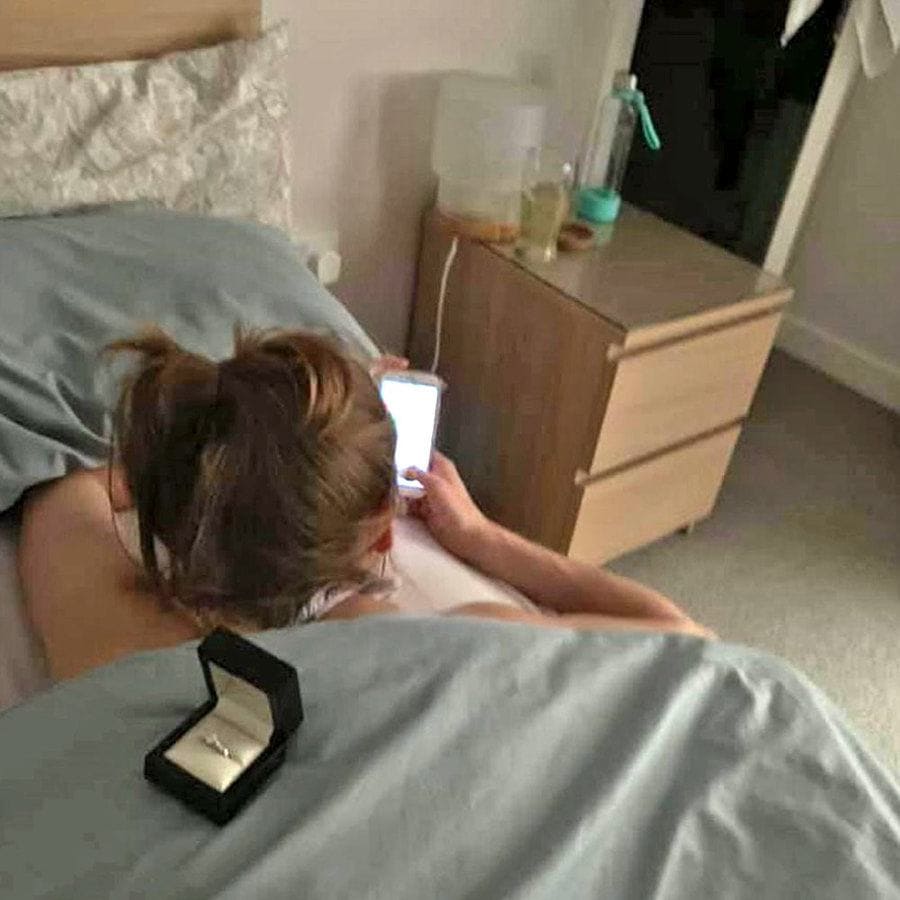 Cally on her stomach, looking at her phone with the engagement ring sitting on her back. 