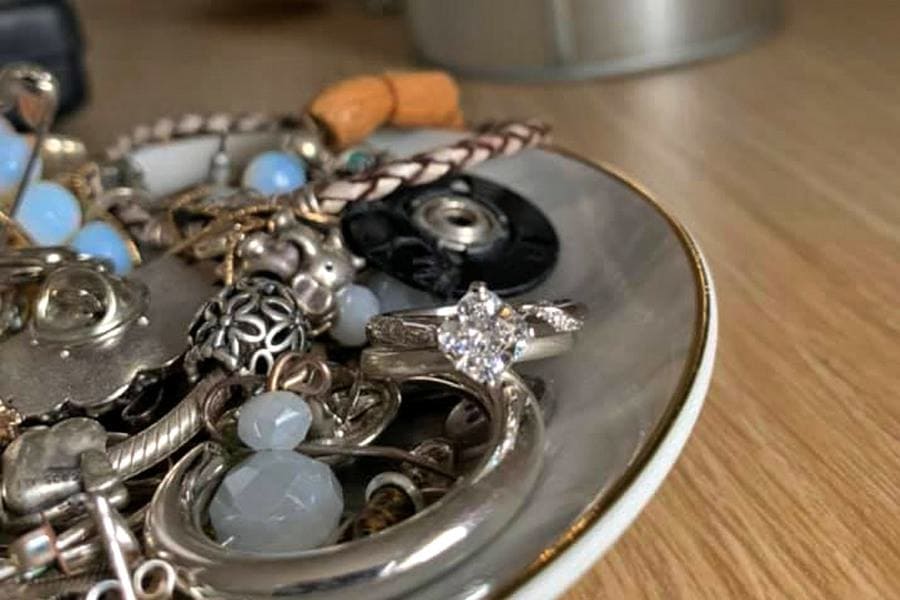 The engagement ring is sitting on top of a pile of jewelry, which is in a marble dish. 