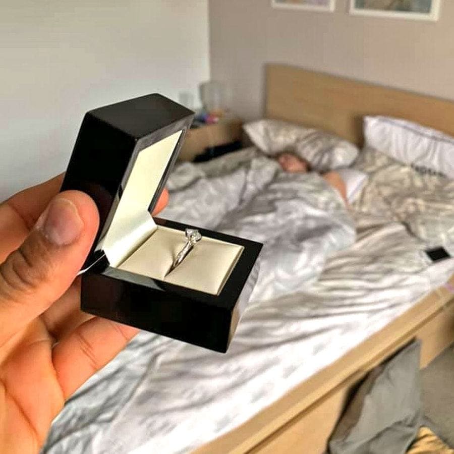 Photo of the engagement ring in a box with Cally lying in bed behind it. 