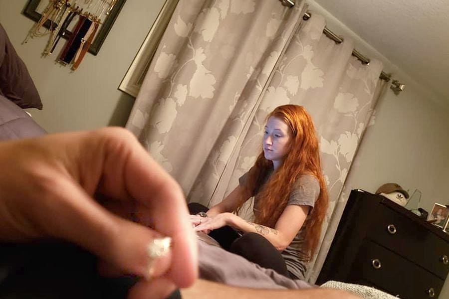 Danielle is sitting on the bed, browsing on her laptop with Colton’s hand in the corner of the photo holding the engagement ring. 