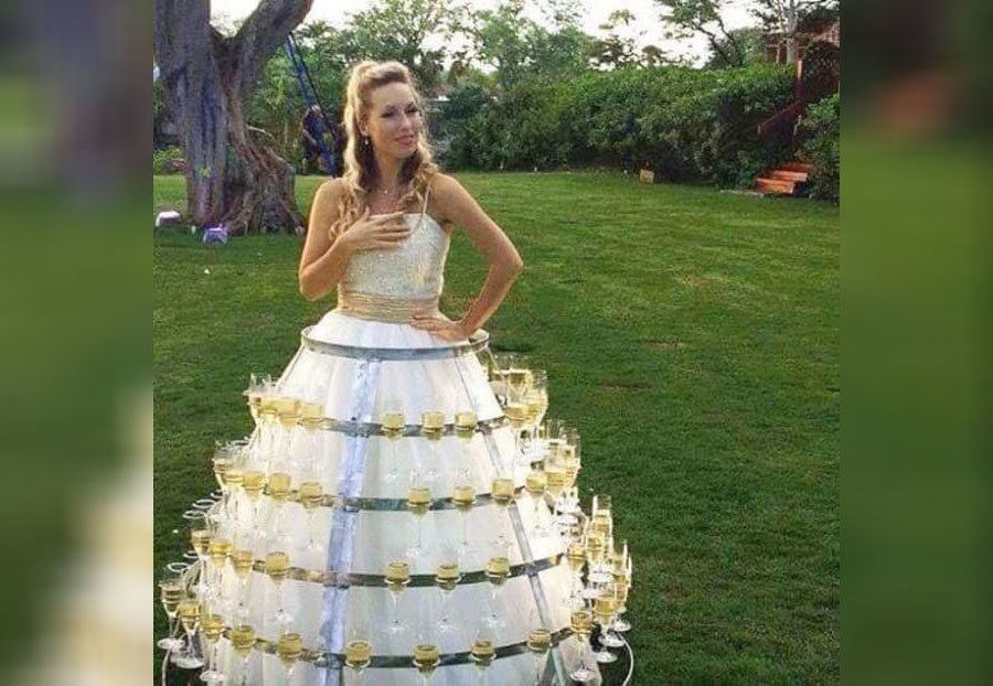 A wedding dress holding a bunch of glasses of wine