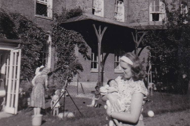 Photograph of a young mother in her back yard holding a baby. 