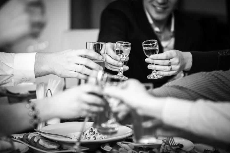 Closeup black and white photo of hands clinking glasses at the restaurant. 