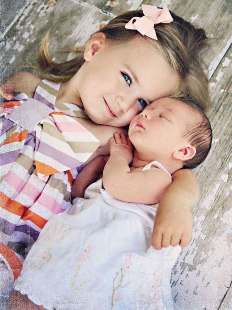Toddler girl hugged together with a sleeping newborn baby girl. 