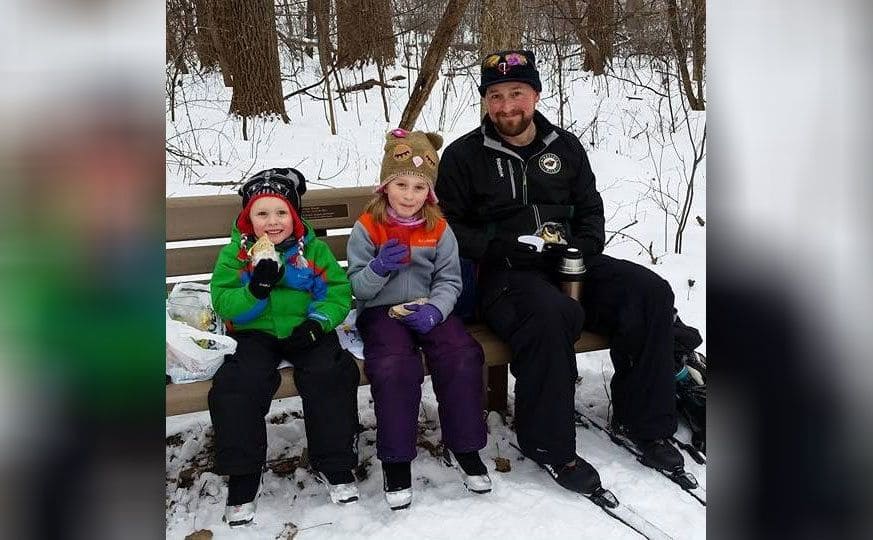 Saga sits on a bench beside her dad and brother