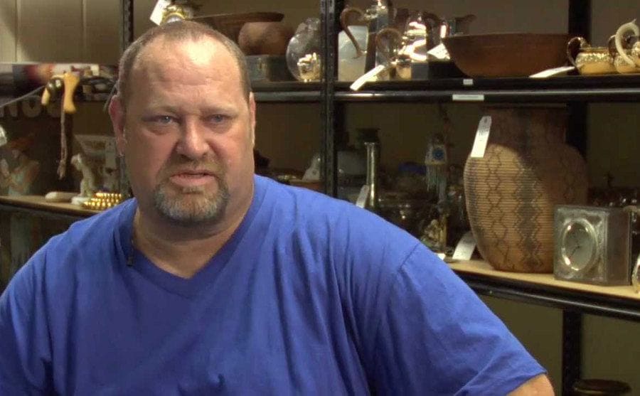 Loren Krytzer is sitting in front of a shelf of antiques. 