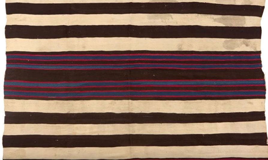 A photograph of the blanket which is white and black striped with smaller red, black, green, and orange stripes. 