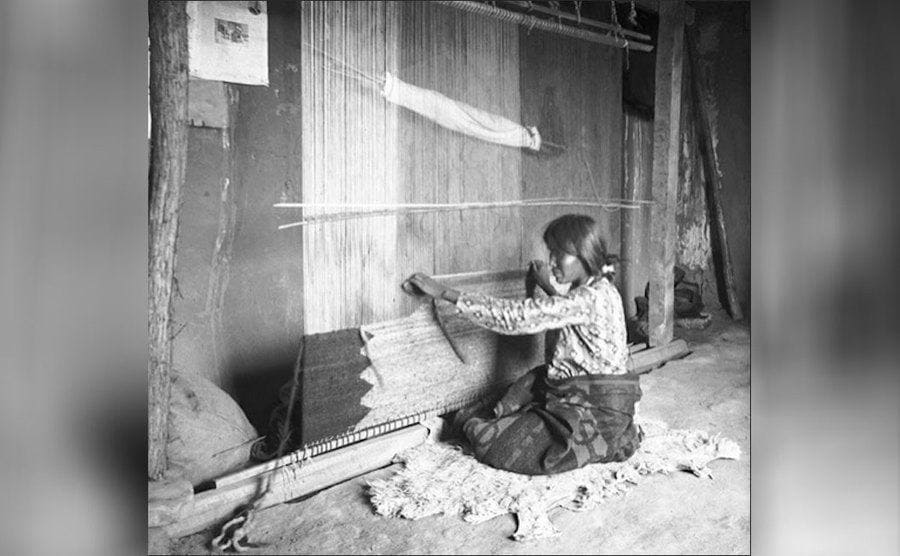 A woman weaving strings of fabric 