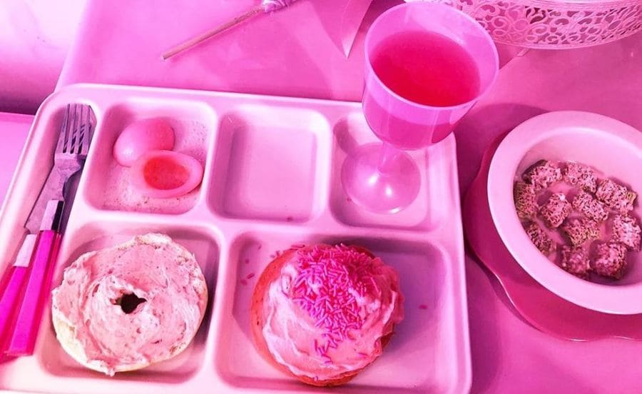 A pink tray of pink foods, including a pink bagel with pink cream cheese, a pink hard-boiled egg, and a pink toast with cheese and pink sprinkles on it. 