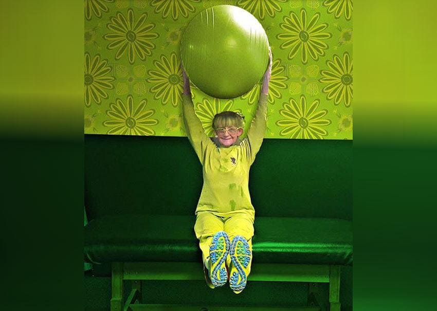 Elizabeth Sweetheart dressed in all green, holding a green ball and sitting on a large green table. 