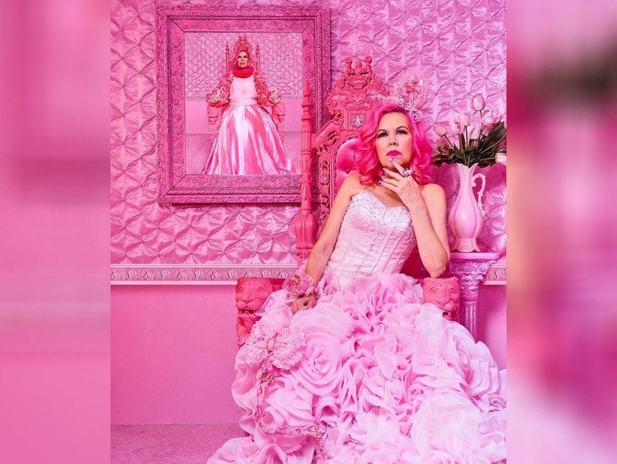 Kitten Kay Sera sitting on her throne in front of a framed photograph of her sitting on her throne, all in pink