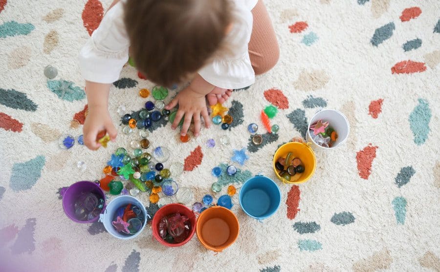 A toddler is playing with beads in different colored buckets