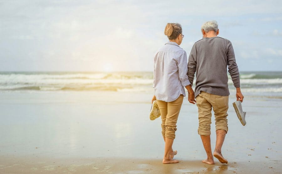 A blonde woman and a man are walking along the beach holding hands at sunrise
