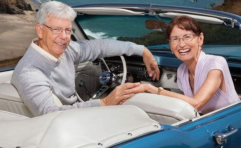 Janice and Prentiss sitting in a convertible in front of the beach 