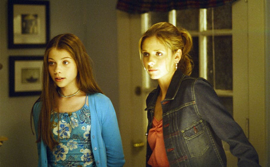 Michelle Trachtenberg and Sarah Michelle Gellar standing in a dimly lit entranceway to a home