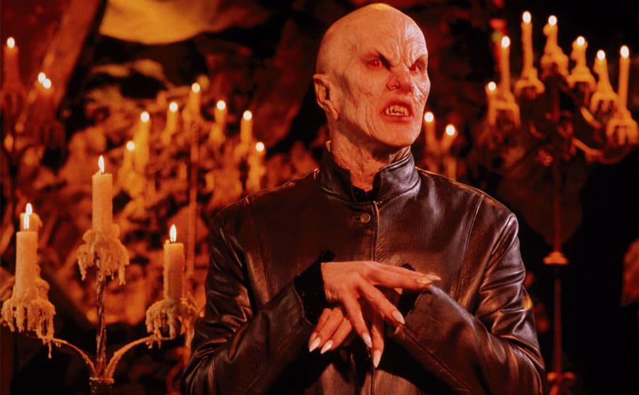 Mark Metcalf in Buffy the Vampire Slayer standing in a dark cave-like room with candles lit around him