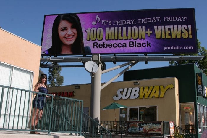 Rebecca black posing next to her billboard