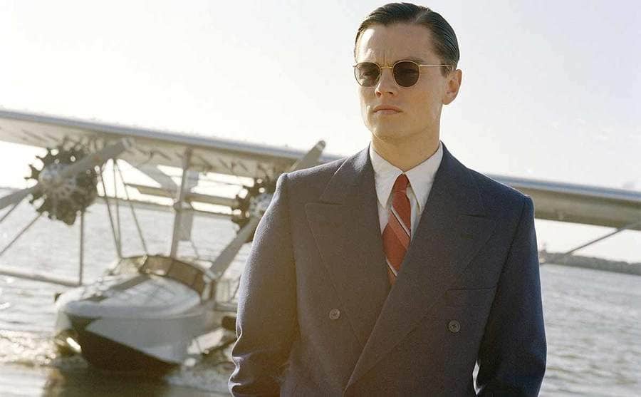 Leonardo DiCaprio standing on the beach with his plane in the water behind him