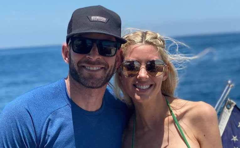 Tarek and Heather posing together on a yacht with the ocean and the corner of an American flag in view