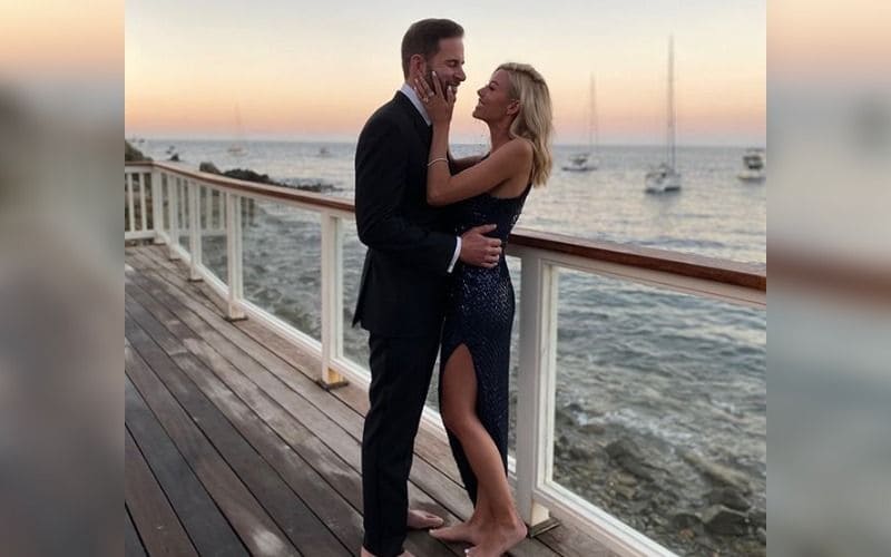 Tarek and Heather posing with big smiles on their faces on a wooden deck overlooking the ocean
