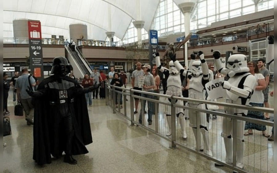 A guy dressed as Darth Vader heading for Comic-Con waving Stormtroopers fans