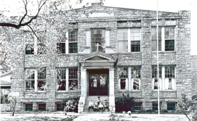 An old orphanage with kids sitting on the front steps