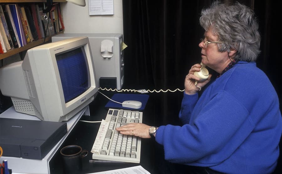 An older woman using an old computer to look stuff up while on the phone