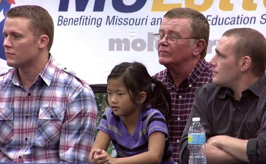 Mark Hill with his daughter on his lap and his sons around him being interviewed