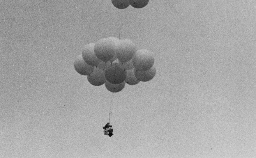 A close-up photograph of Larry in his chair attached to balloons