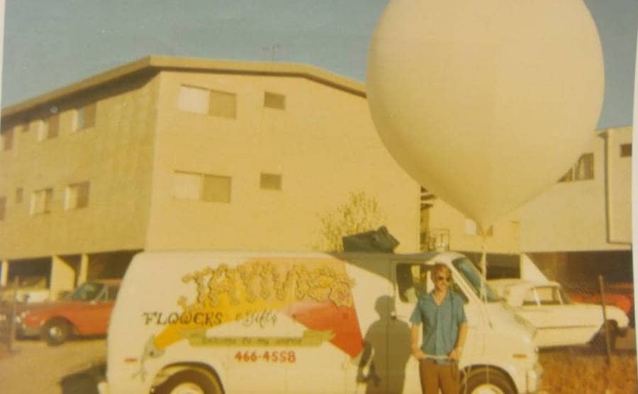 Larry standing outside of his apartment complex in front of a van with a weather balloon next to him
