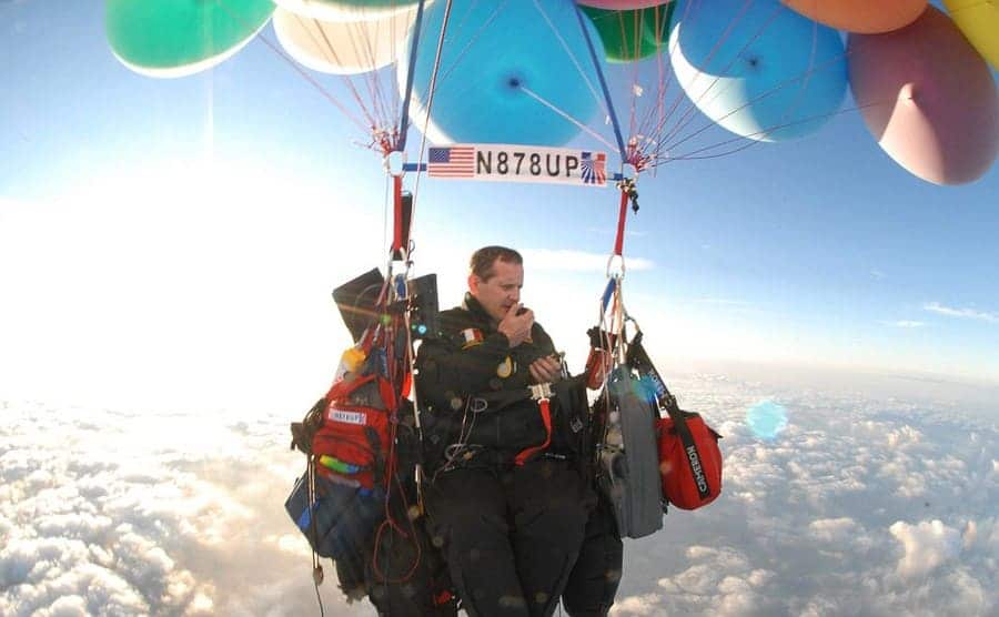Jonathan Trappe tied to colorful weather balloons over clouds