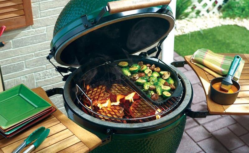 A photograph of the big green egg opened up with steak and vegetables grilling