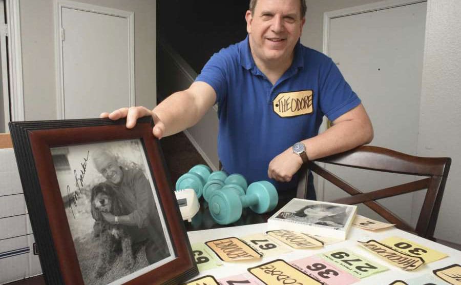 Ted Slauson with his name tag on propping up an autographed photo of Bob Barker with his winnings and name tags laid out on the table