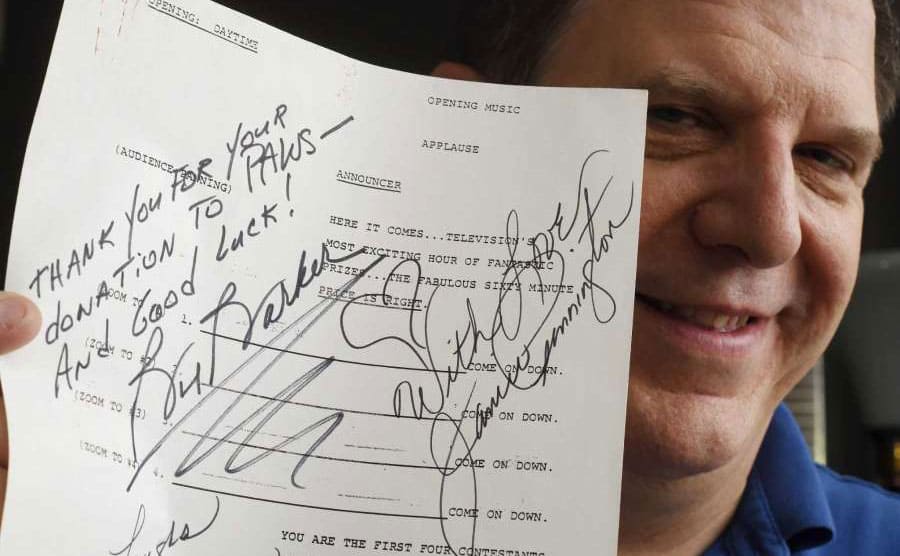Ted holding a signed sheet of paper announcing who are the first four contestants with a signature from Bob Barker