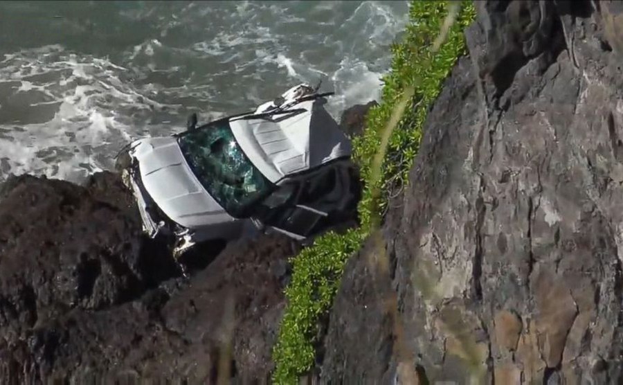 The white SUV crushed on the rocks at the bottom of a cliff