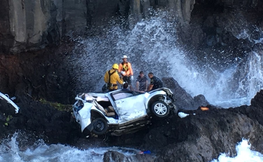 Crew working around the crushed car in the rocky water