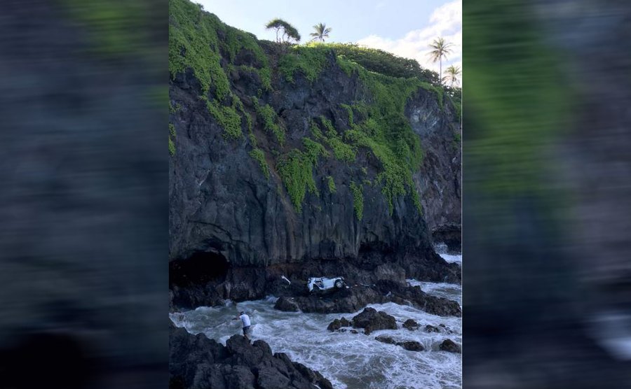 The car at the bottom of a large cliff in rocks covered in water