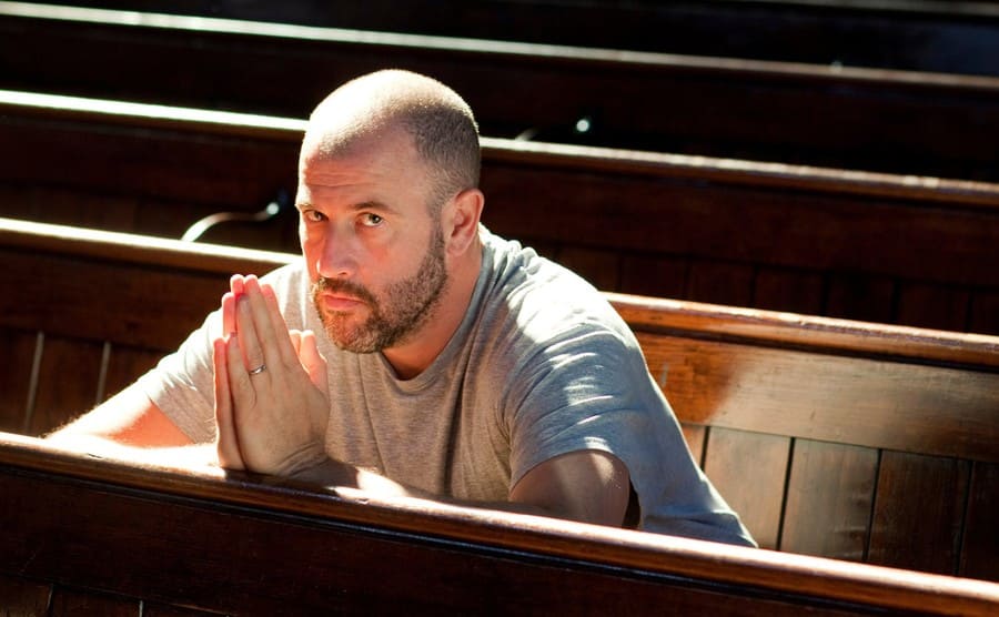 James Frey sitting in a church pew with the palm of his hands pressed together