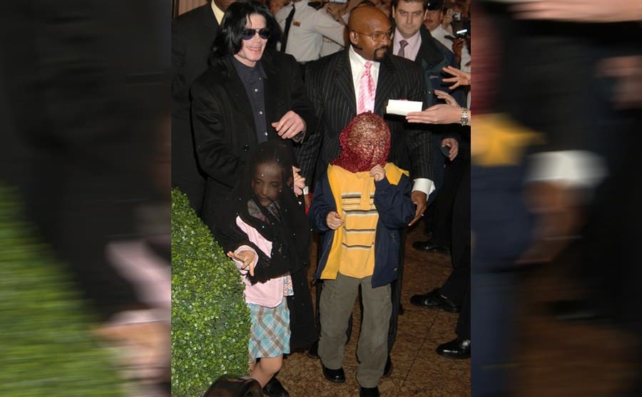 Michael Jackson surrounded by paparazzi with Paris and Prince Michael Jr wearing masks