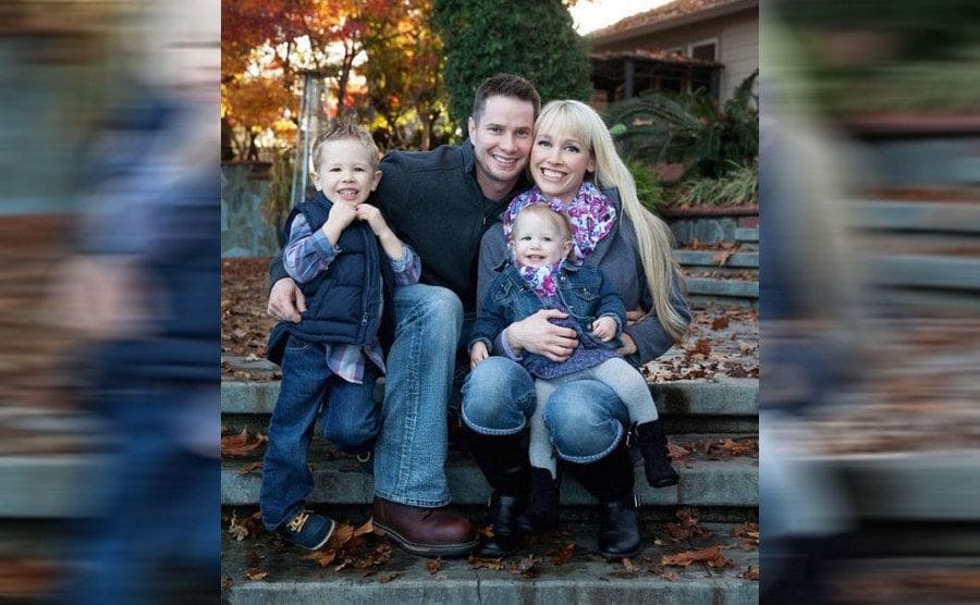 Sherri and Keith Papini sitting on stairs hugging with their two little children