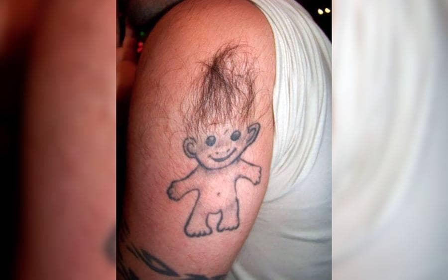 A tattoo of a troll on a guy's arm with hair attached to it