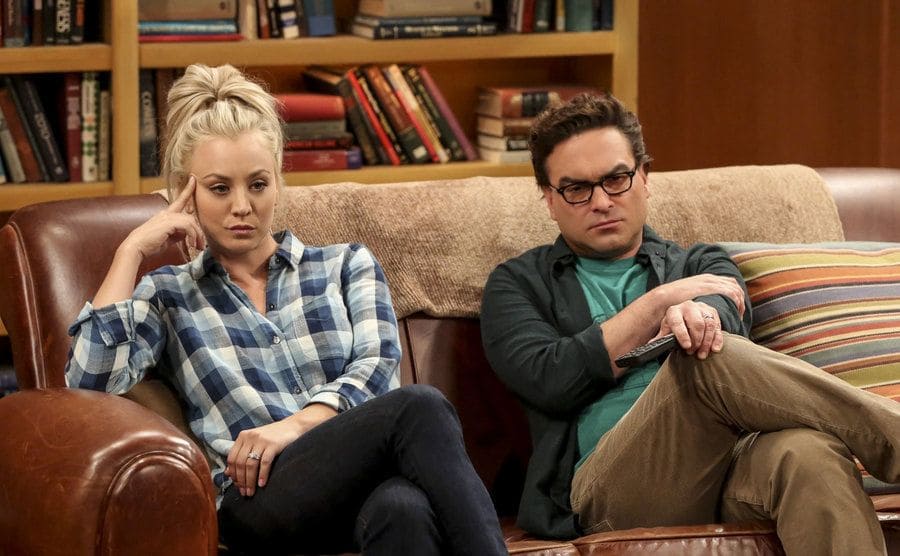 Kaley Cuoco and Johnny Galecki sitting on the brown leather couch in the living room on the set of the Big Bang Theory